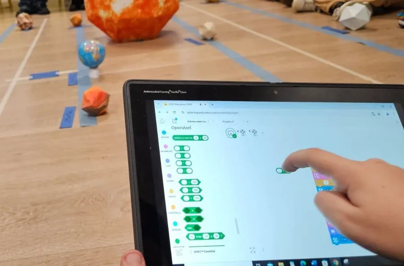 Tablet con la programmazione a blocchi e, sul pavimento, i pianeti del sistema solare costruiti in carta.
