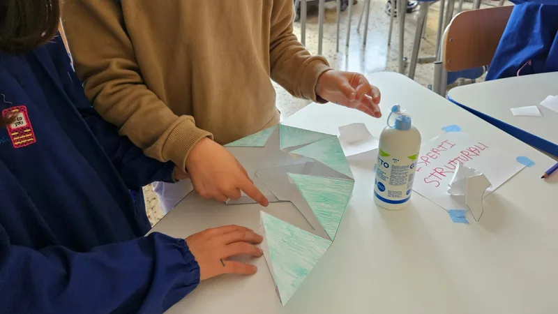 Mani di studenti che assemblano una struttura di carta piegata.